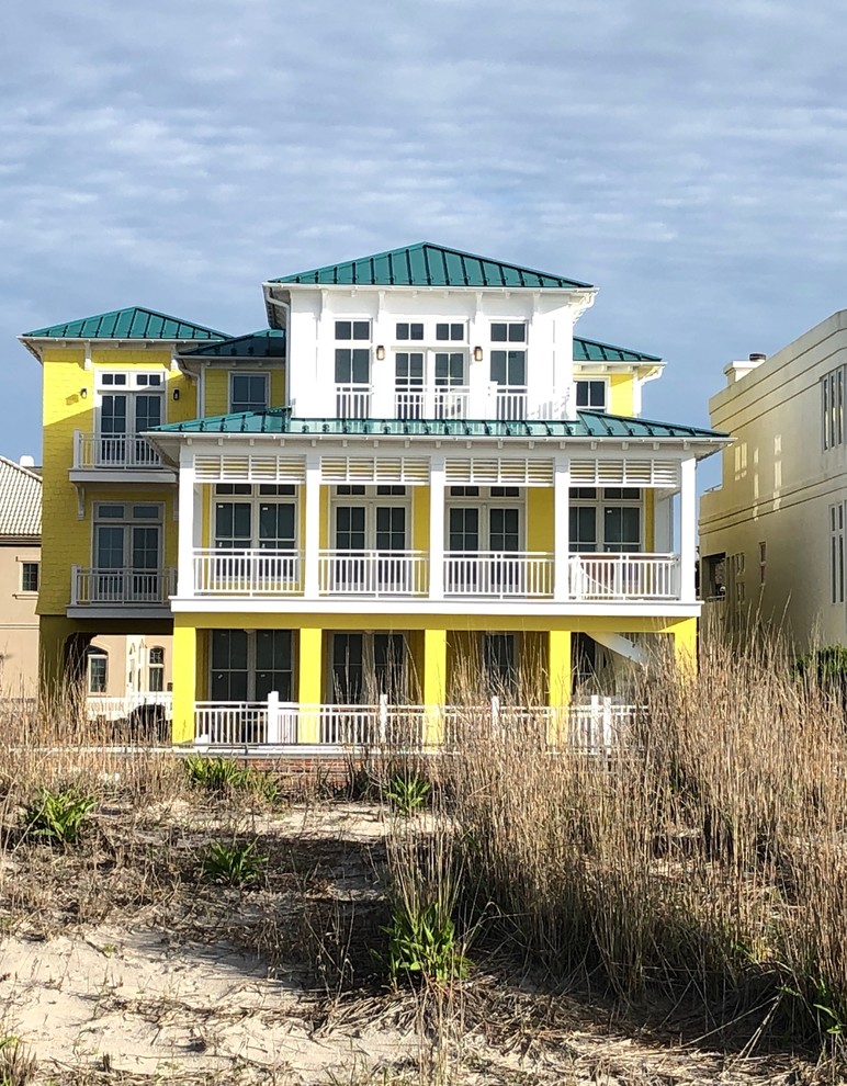 Imagen de fachada de casa amarilla exótica grande de tres plantas con revestimiento de aglomerado de cemento, tejado a cuatro aguas y tejado de metal