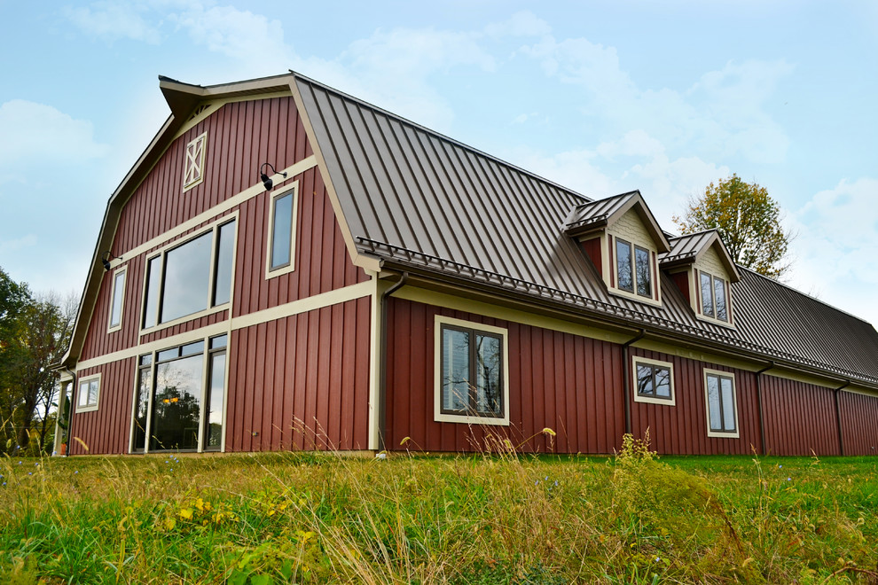Foto della facciata di una casa rossa country a due piani con tetto a mansarda e rivestimento in legno