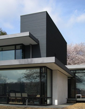 Cette image montre une grande façade de maison grise minimaliste en béton à un étage avec un toit plat.