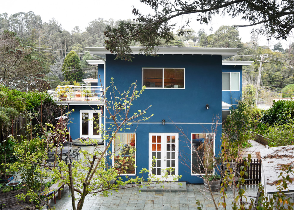 Aménagement d'une façade de maison bleue moderne en stuc de taille moyenne et à un étage avec un toit plat et un toit mixte.