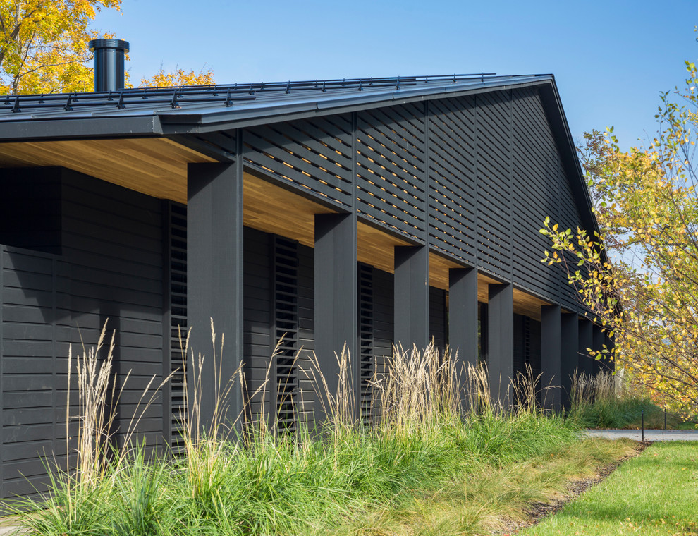 На фото: большой, одноэтажный, деревянный, черный частный загородный дом в современном стиле с двускатной крышей и металлической крышей