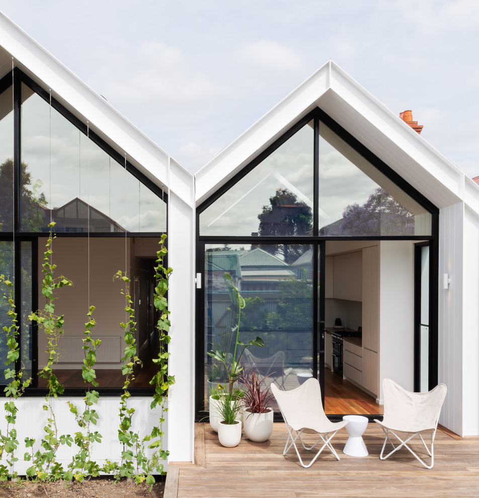 Imagen de fachada de casa blanca nórdica pequeña de una planta con revestimiento de aglomerado de cemento, tejado a dos aguas y tejado de metal