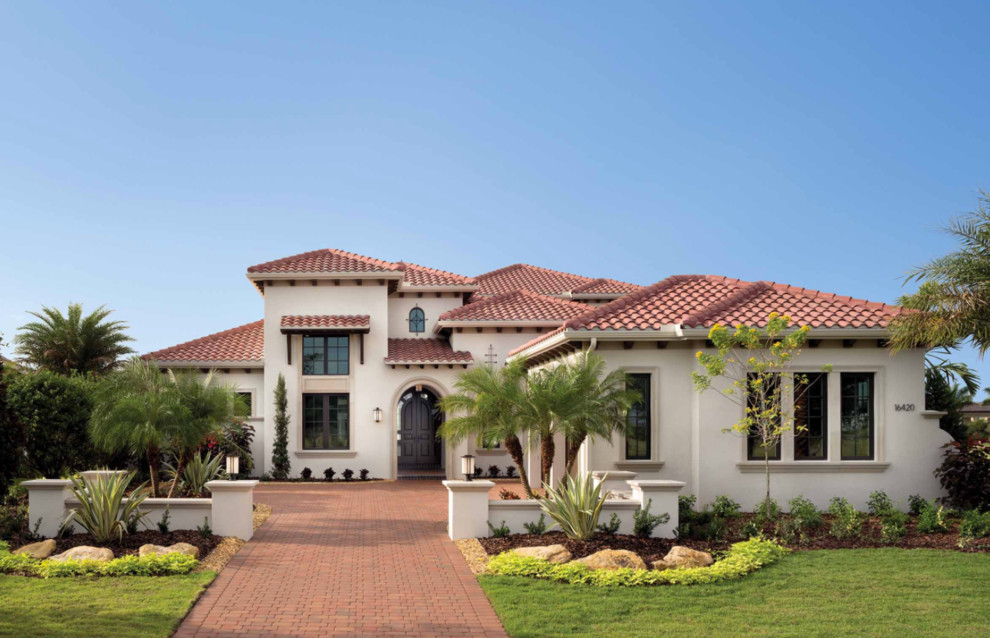 Example of a huge beach style beige two-story stucco house exterior design in Miami with a clipped gable roof and a tile roof