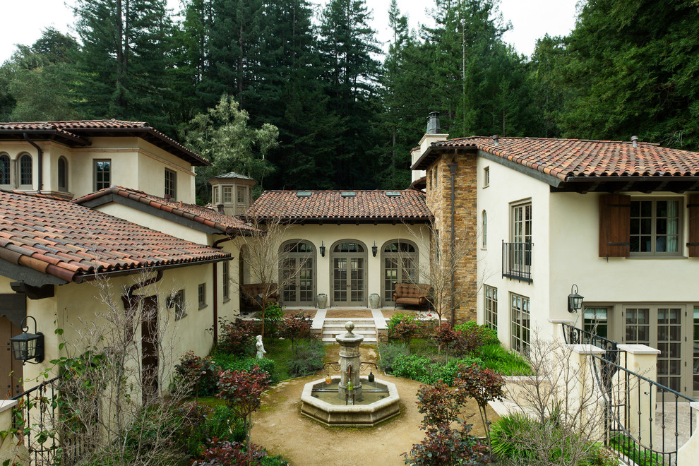 Cette image montre une grande façade de maison blanche méditerranéenne en stuc à un étage avec un toit à deux pans et un toit en tuile.