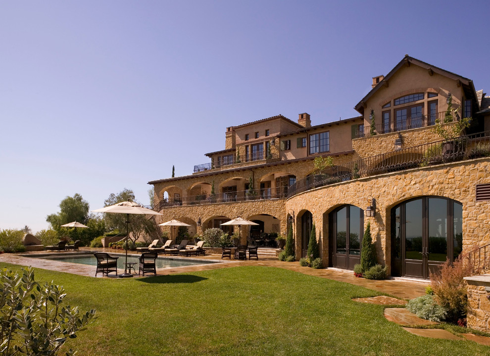 Example of a large tuscan beige three-story stone exterior home design in Orange County