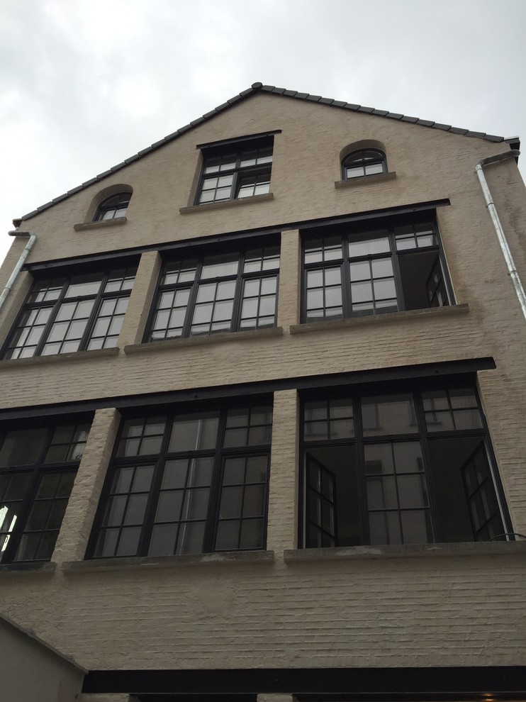 Ejemplo de fachada de piso beige urbana de tamaño medio de tres plantas con revestimiento de ladrillo y tejado a dos aguas