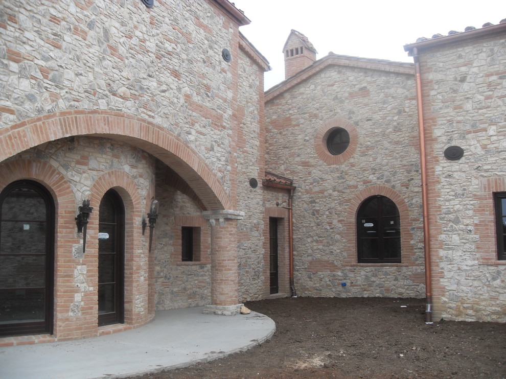Cette photo montre une grande façade de maison beige méditerranéenne en brique à un étage avec un toit à deux pans et un toit en tuile.