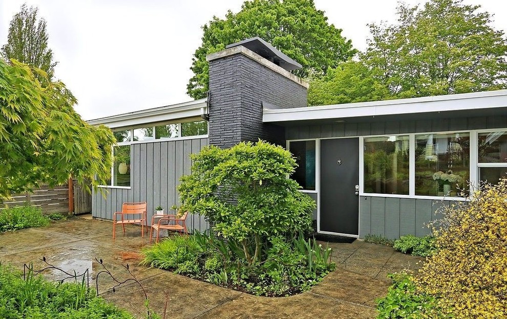 Cette image montre une façade de maison grise vintage en bois de taille moyenne et à un étage avec un toit plat.