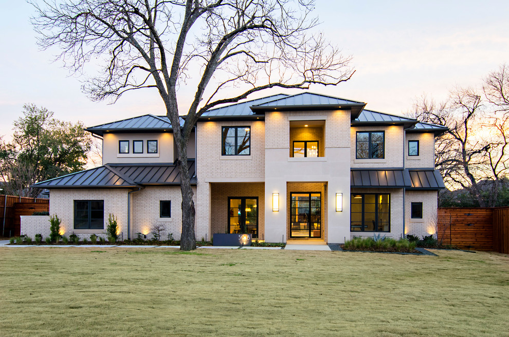 Cette photo montre une façade de maison beige chic en brique à un étage avec un toit à quatre pans et un toit en métal.