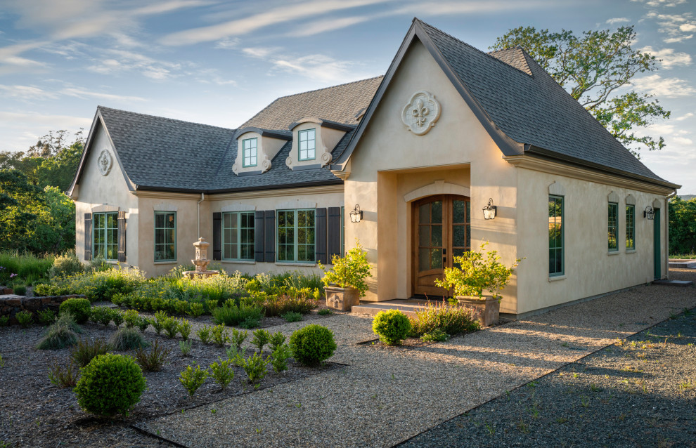 Diseño de fachada de casa beige de tamaño medio de una planta con revestimiento de estuco, tejado a dos aguas y tejado de teja de madera