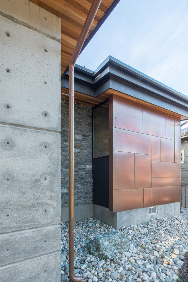 Foto della facciata di una casa piccola grigia moderna a un piano con rivestimento in cemento e copertura in metallo o lamiera