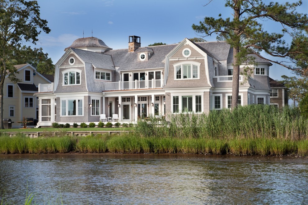 Diseño de fachada beige costera grande de tres plantas con revestimiento de madera y tejado a doble faldón