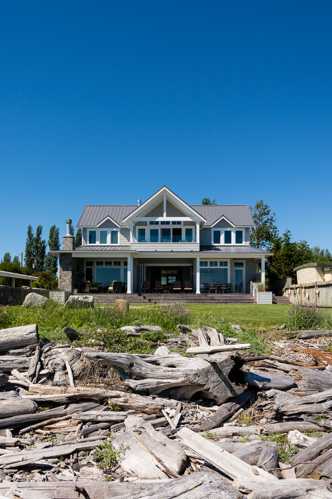Cette photo montre une façade de maison grise bord de mer en panneau de béton fibré de taille moyenne et à un étage avec un toit à deux pans et un toit en métal.