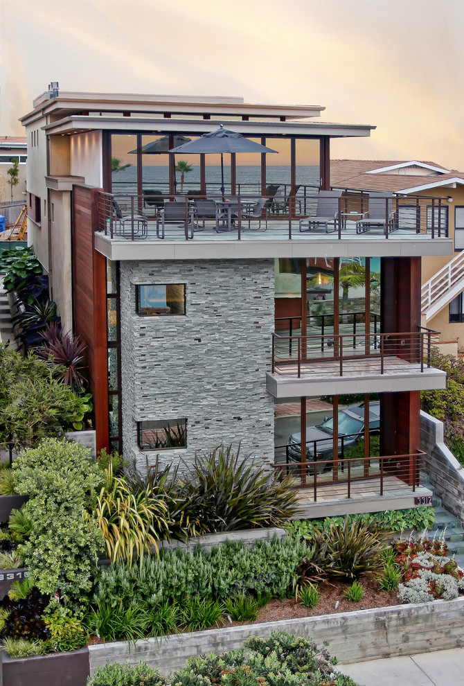 На фото: большой, трехэтажный, серый дом в морском стиле с облицовкой из камня и плоской крышей с