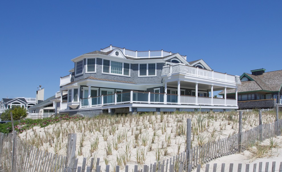 This is an example of an expansive and gey coastal house exterior in New York with three floors, wood cladding and a pitched roof.