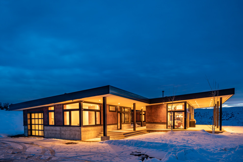 На фото: одноэтажный, коричневый частный загородный дом среднего размера в стиле модернизм с облицовкой из металла, односкатной крышей и металлической крышей