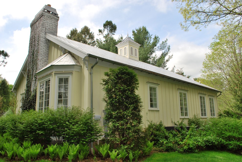 Cette image montre une façade de maison jaune traditionnelle en béton de taille moyenne et de plain-pied avec un toit à deux pans.