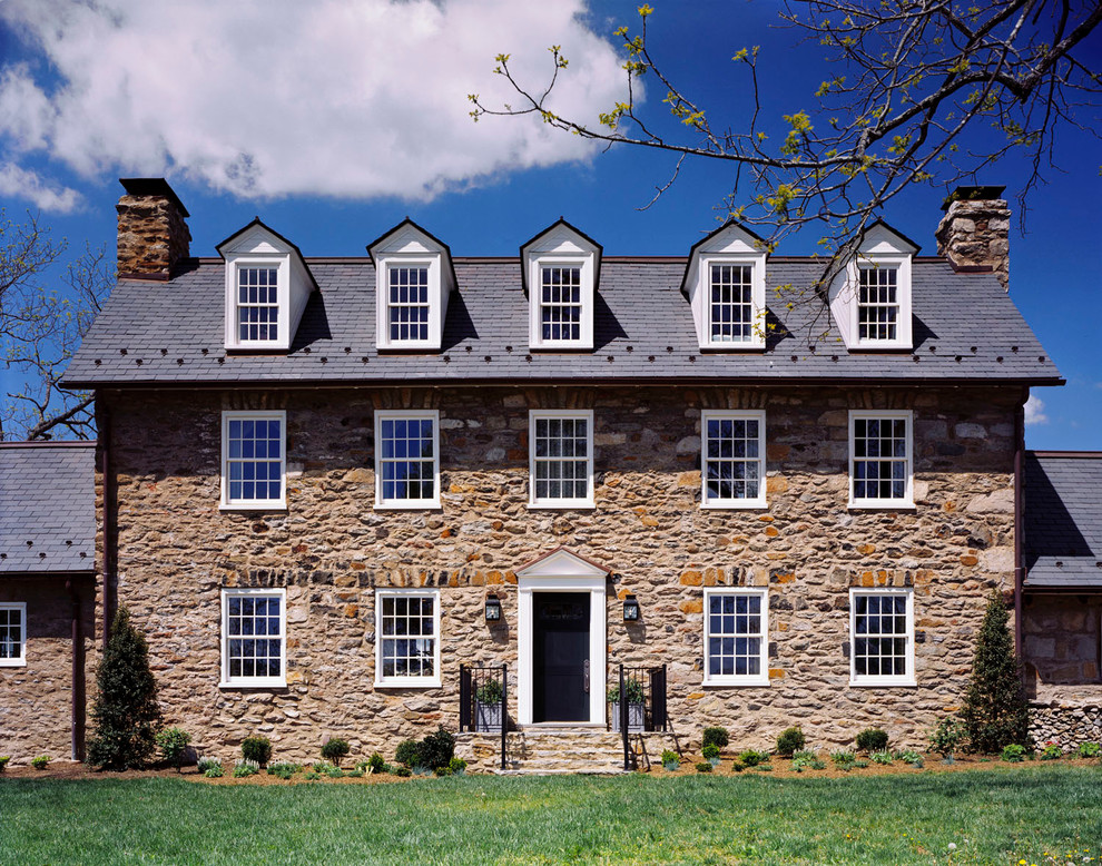 Immagine della facciata di una casa country a tre piani con rivestimento in pietra e tetto a capanna