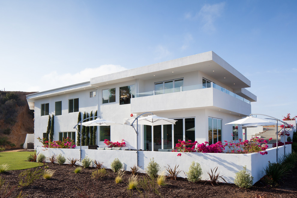 Пример оригинального дизайна: большой, двухэтажный, белый частный загородный дом в современном стиле с облицовкой из цементной штукатурки и плоской крышей