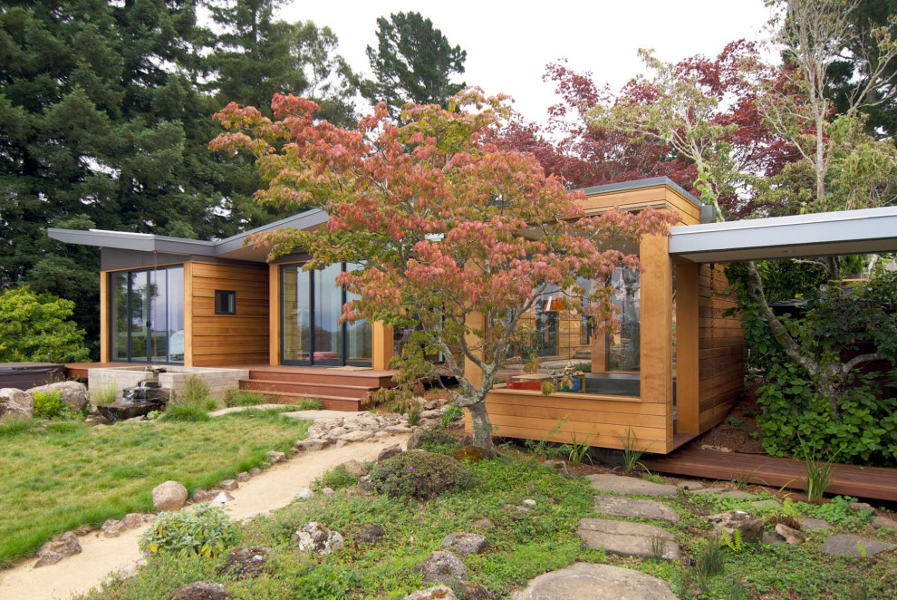 Foto della villa marrone moderna a un piano di medie dimensioni con rivestimento in legno, tetto a farfalla, pannelli e listelle di legno, copertura verde e tetto grigio