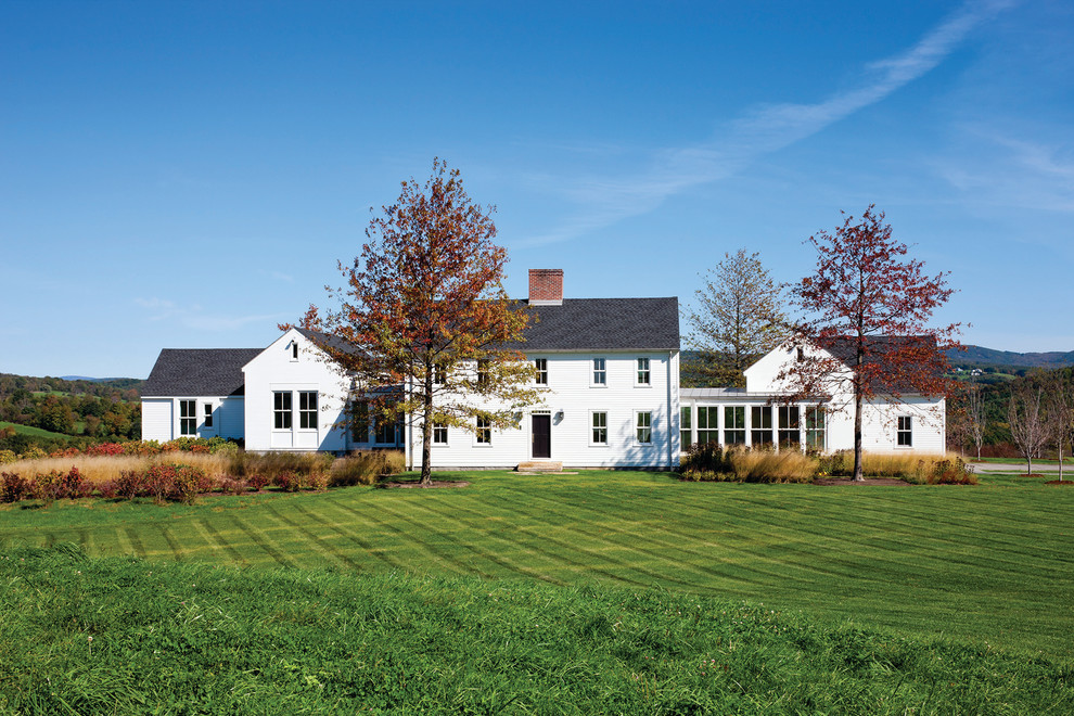 Foto della facciata di una casa grande bianca country a due piani con tetto a capanna e rivestimento in legno