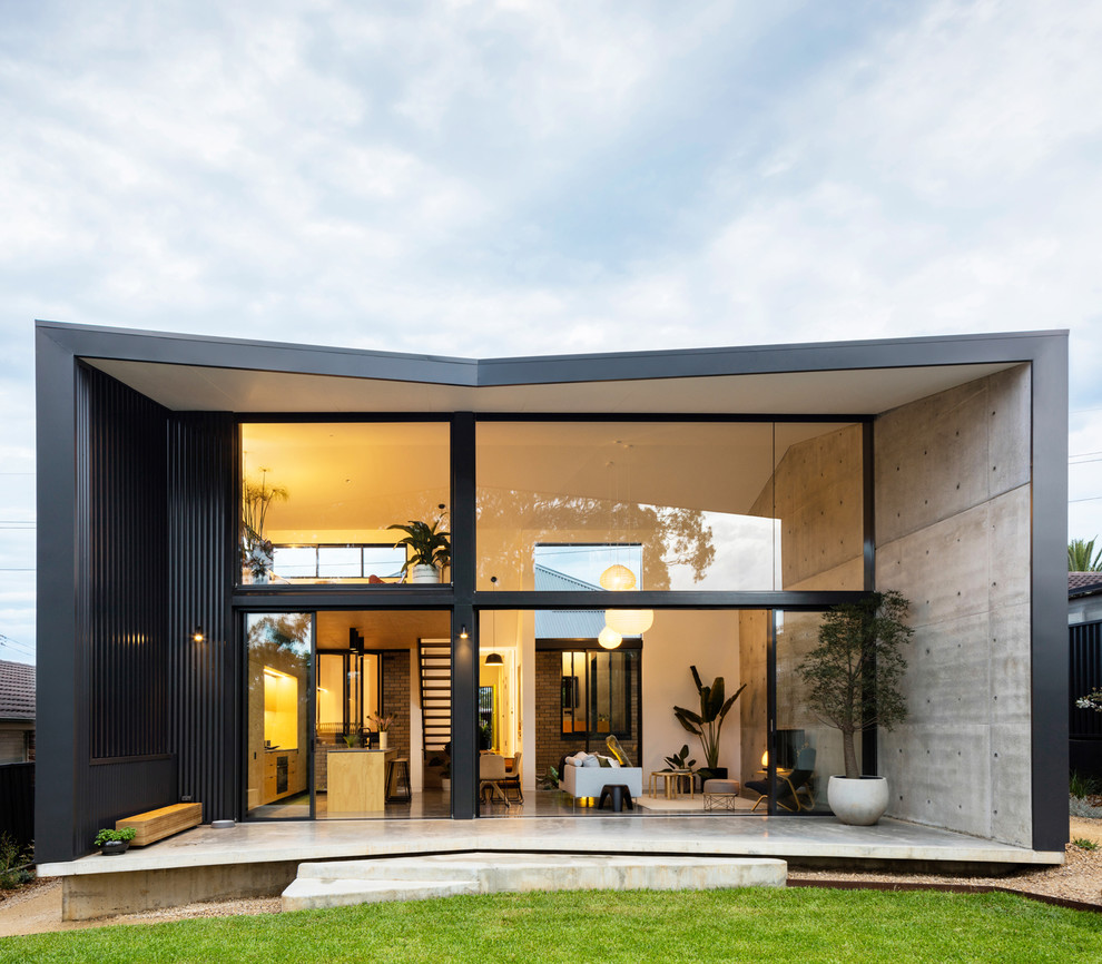 Aménagement d'une façade de maison noire moderne en béton à un étage avec un toit à deux pans.