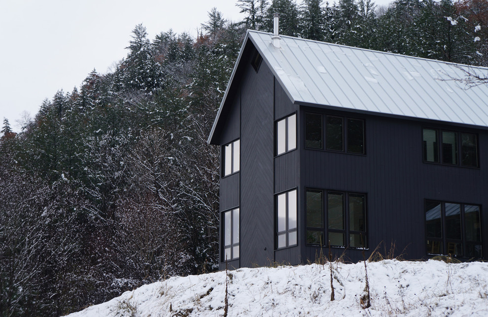 Aménagement d'une façade de maison noire contemporaine en bois de taille moyenne et à un étage avec un toit à deux pans et un toit en métal.