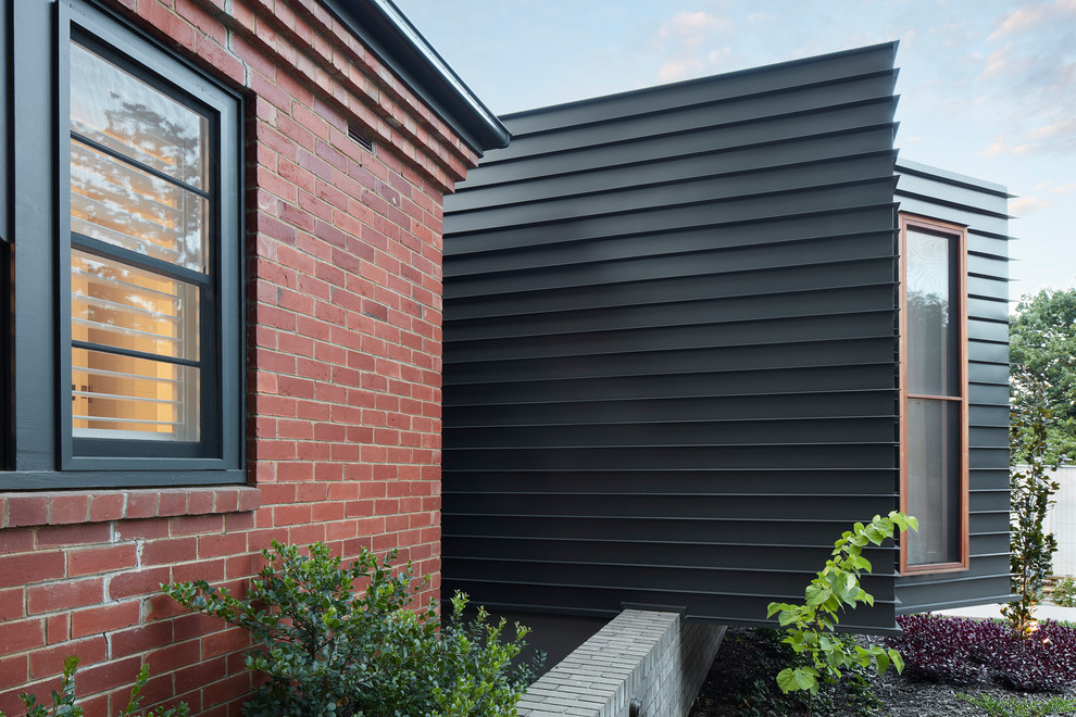 Réalisation d'une façade de maison métallique et noire design de taille moyenne et de plain-pied avec un toit plat et un toit en métal.