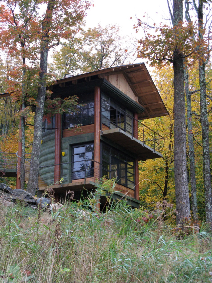 На фото: двухэтажный, маленький, зеленый дом в стиле рустика с облицовкой из бетона, двускатной крышей и металлической крышей для на участке и в саду