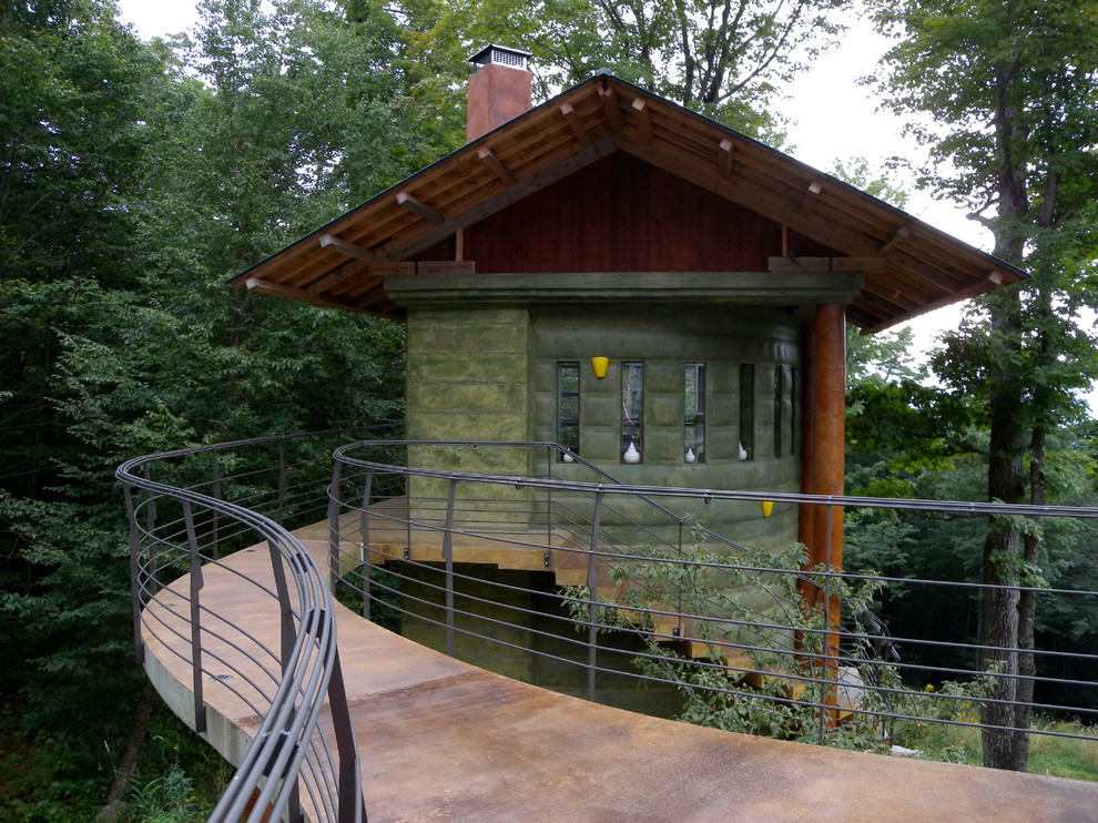 Cette image montre une petite façade de maison verte chalet en béton à un étage avec un toit à deux pans et un toit en métal.