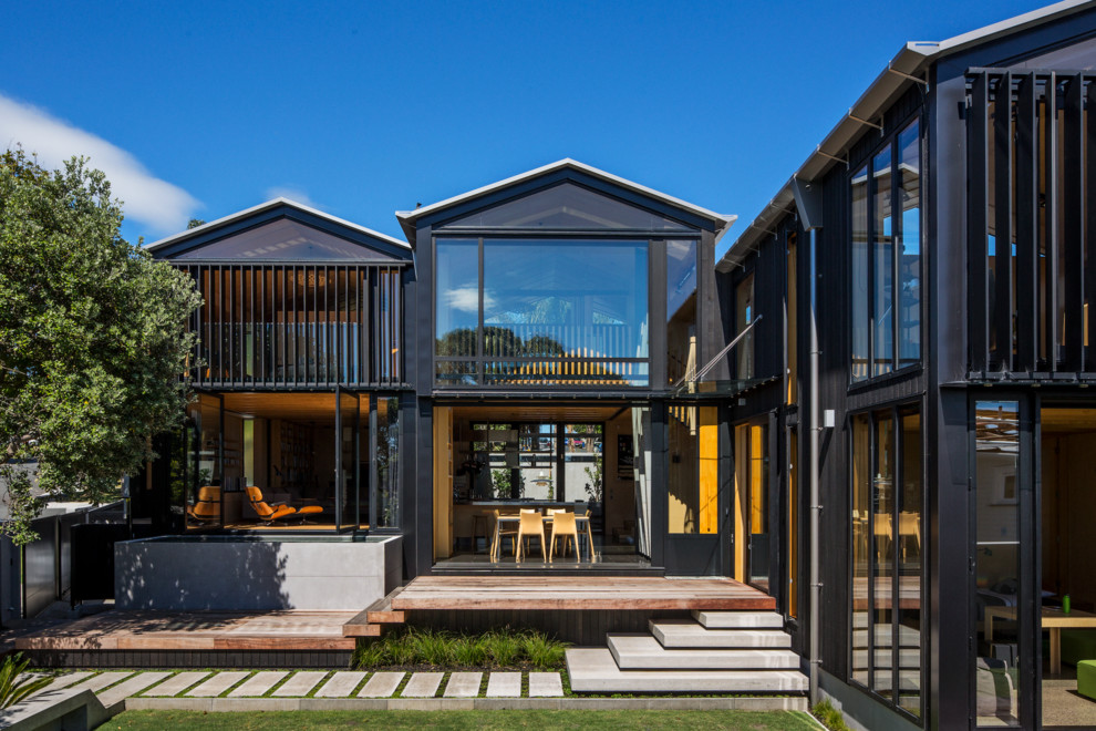 Black contemporary two floor house exterior in Auckland with wood cladding and a pitched roof.