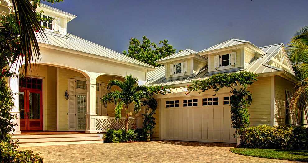Immagine della villa gialla tropicale a un piano di medie dimensioni con rivestimento in legno, tetto a padiglione e copertura in metallo o lamiera