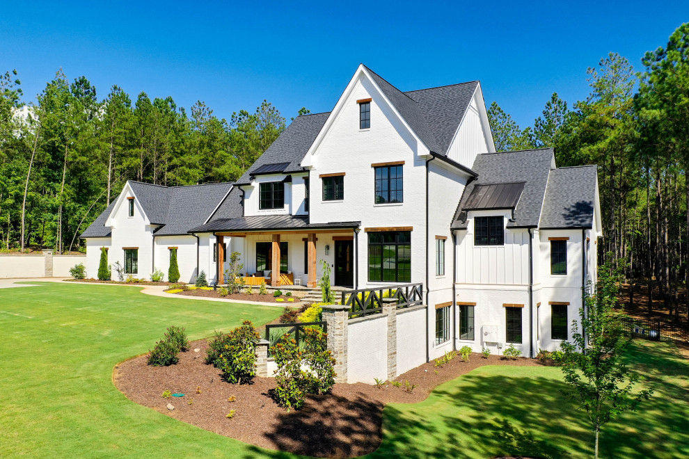 Foto della villa grande bianca country a tre piani con rivestimento in mattone verniciato, copertura mista, tetto nero e pannelli e listelle di legno
