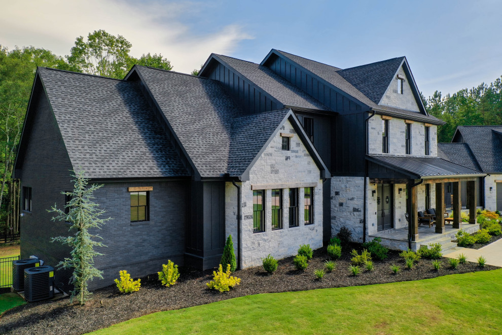 Réalisation d'une très grande façade de maison noire minimaliste en brique et planches et couvre-joints à deux étages et plus avec un toit mixte et un toit noir.