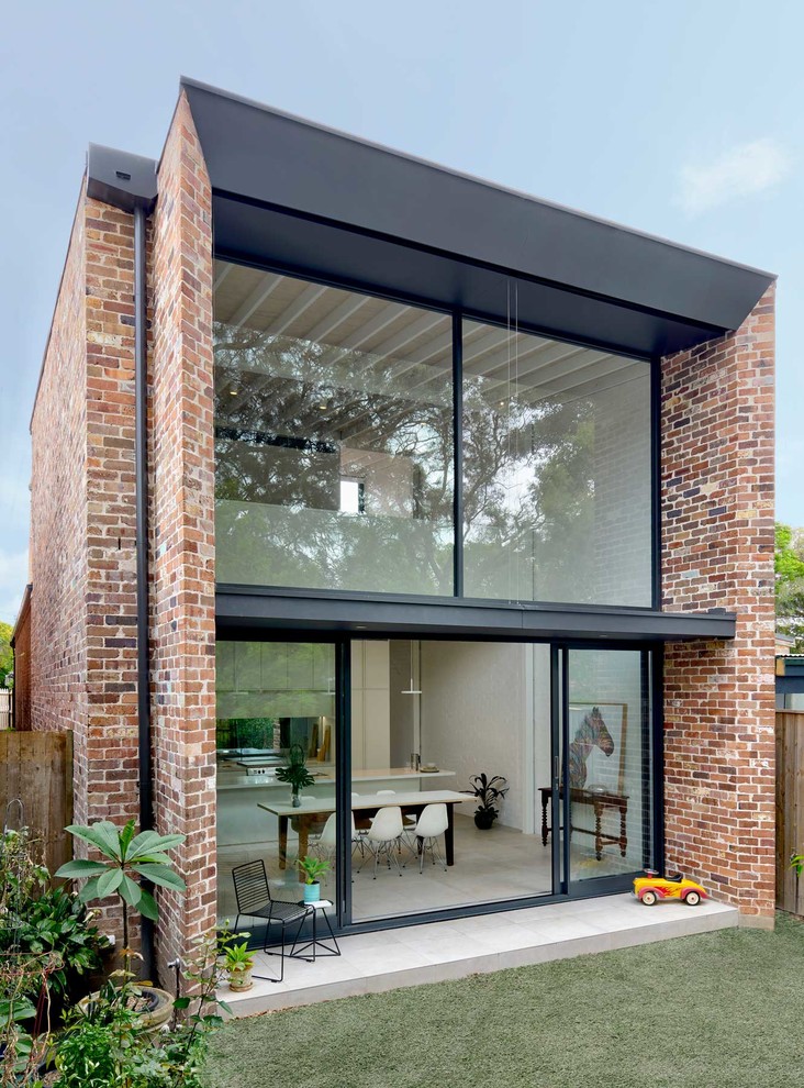 Cette image montre une façade de maison design en brique de taille moyenne et à un étage avec un toit plat et un toit en métal.