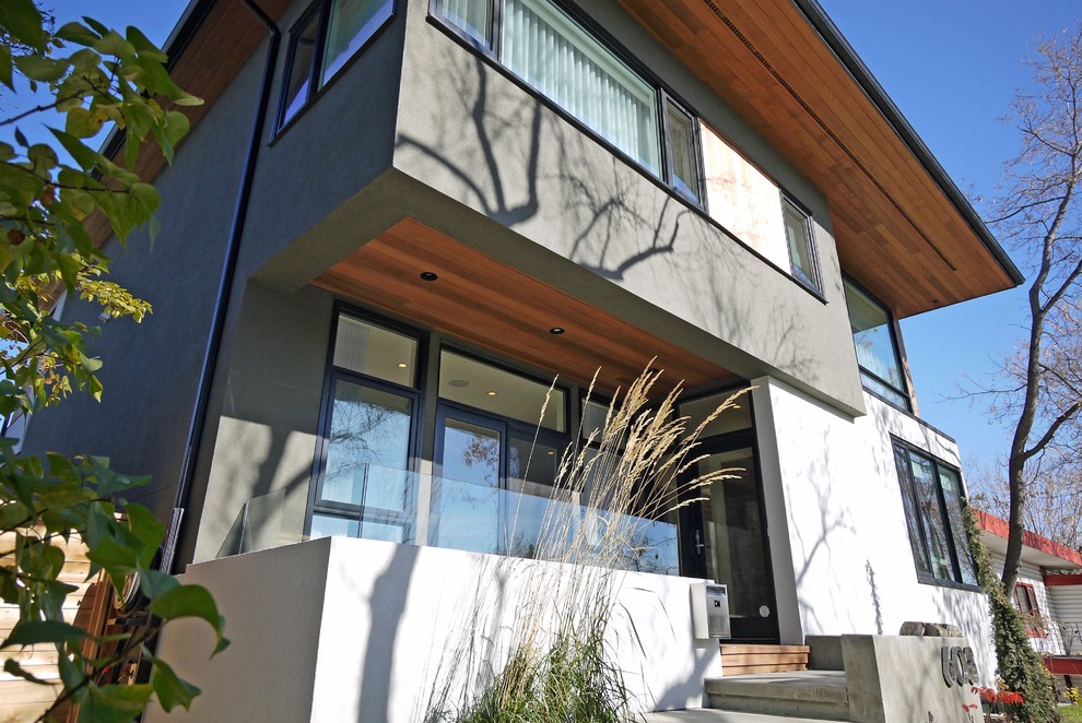 Inspiration pour une façade de maison grise minimaliste en stuc de taille moyenne et à un étage avec un toit à quatre pans.