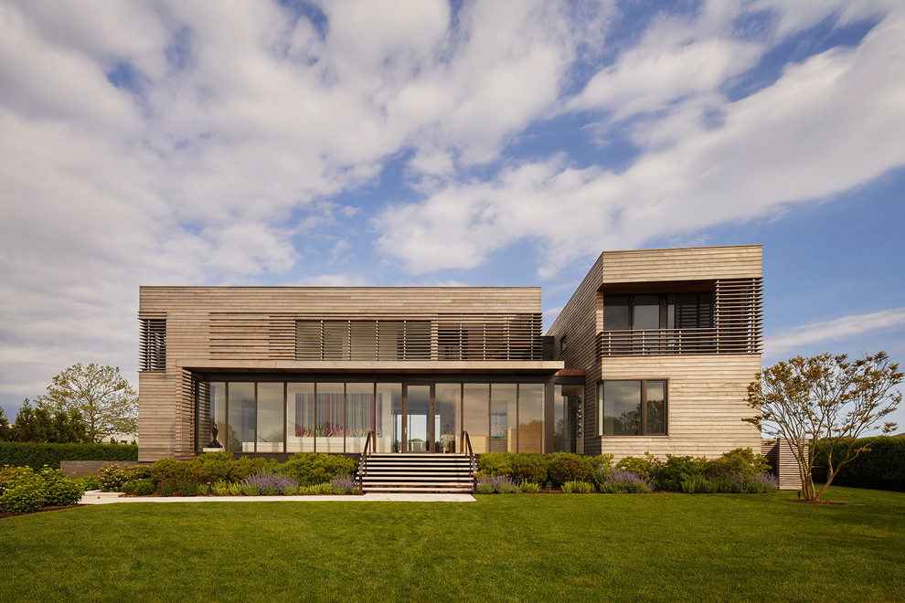 This is an example of an expansive coastal two floor detached house in New York with wood cladding and a flat roof.