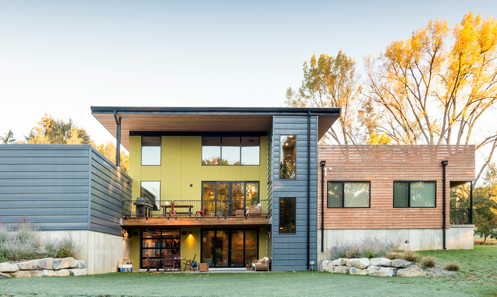 Réalisation d'une grande façade de maison jaune design à un étage avec un toit plat et un revêtement mixte.