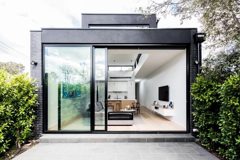 Inspiration pour une petite façade de maison noire minimaliste en brique de plain-pied avec un toit plat et un toit en métal.