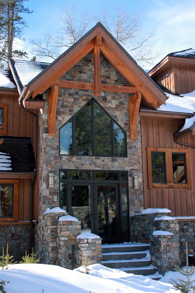Large and brown rustic two floor house exterior in Calgary with stone cladding and a pitched roof.