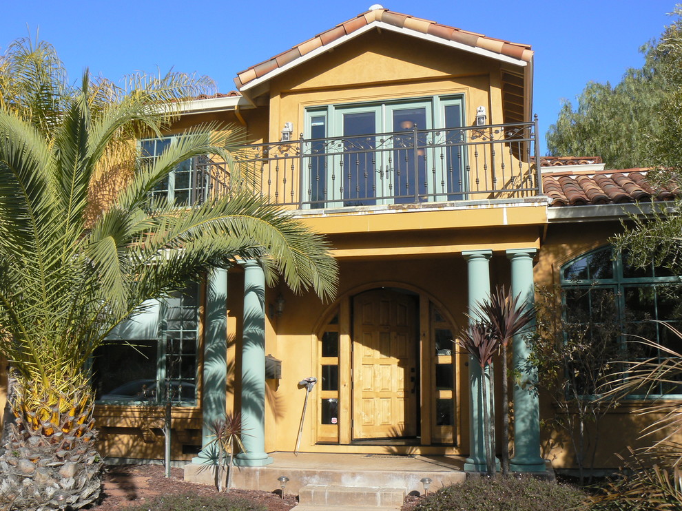 Стильный дизайн: большой, двухэтажный, желтый частный загородный дом в средиземноморском стиле с облицовкой из цементной штукатурки, двускатной крышей и черепичной крышей - последний тренд