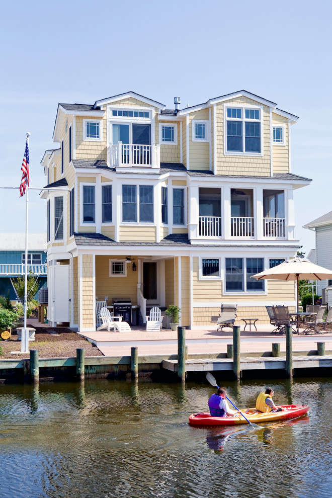 Aménagement d'une grande façade de maison jaune bord de mer à deux étages et plus avec un revêtement en vinyle, un toit à quatre pans et un toit mixte.