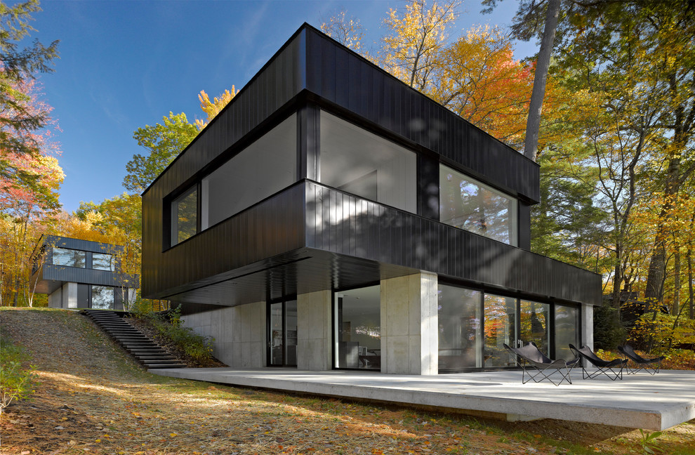 На фото: большой, двухэтажный, черный частный загородный дом в современном стиле с облицовкой из металла, плоской крышей и металлической крышей