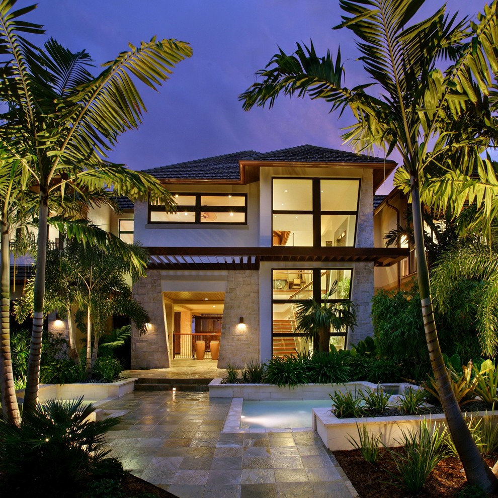 Large island style beige two-story stone house exterior photo in Miami with a hip roof and a shingle roof