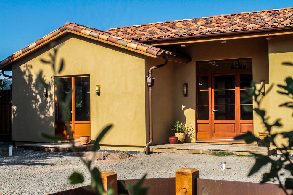 Modelo de fachada de casa beige mediterránea de tamaño medio de una planta con revestimiento de estuco y tejado de teja de madera