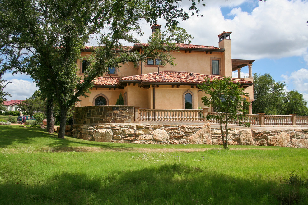 Cette image montre une grande façade de maison beige méditerranéenne en stuc à un étage avec un toit à deux pans et un toit en tuile.