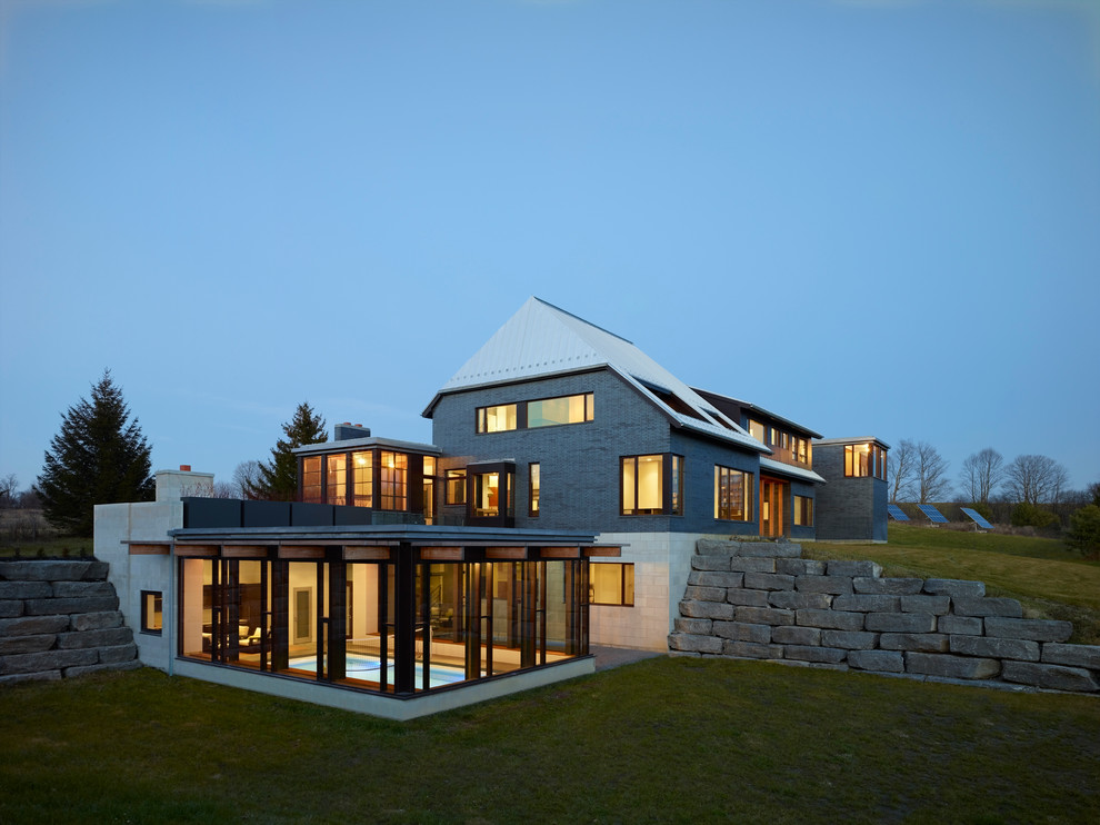 На фото: трехэтажный, большой, серый частный загородный дом в современном стиле с комбинированной облицовкой и полувальмовой крышей с