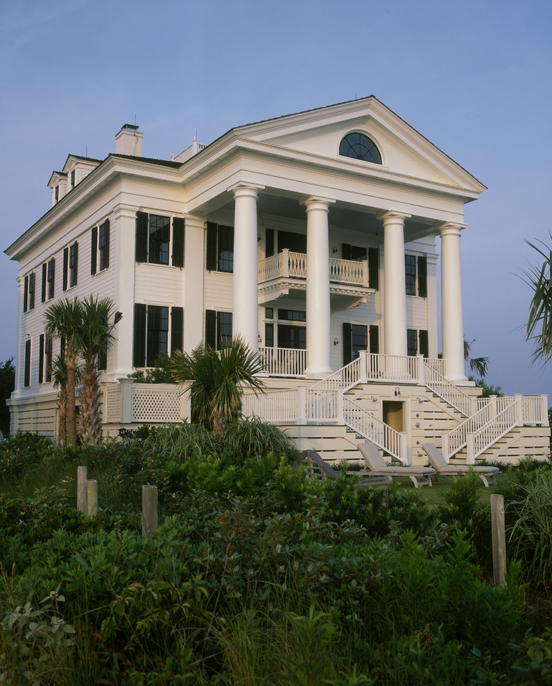 Esempio della facciata di una casa grande bianca classica a tre piani con rivestimento in legno e terreno in pendenza