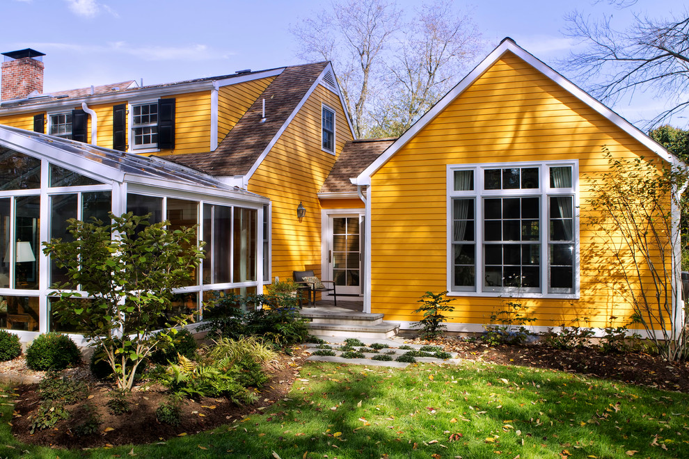 Imagen de fachada de casa amarilla clásica de dos plantas con revestimiento de aglomerado de cemento, tejado a dos aguas y tejado de teja de madera