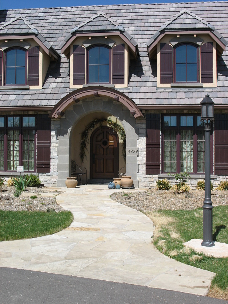 Example of a large classic gray two-story stone house exterior design in Denver with a clipped gable roof and a tile roof